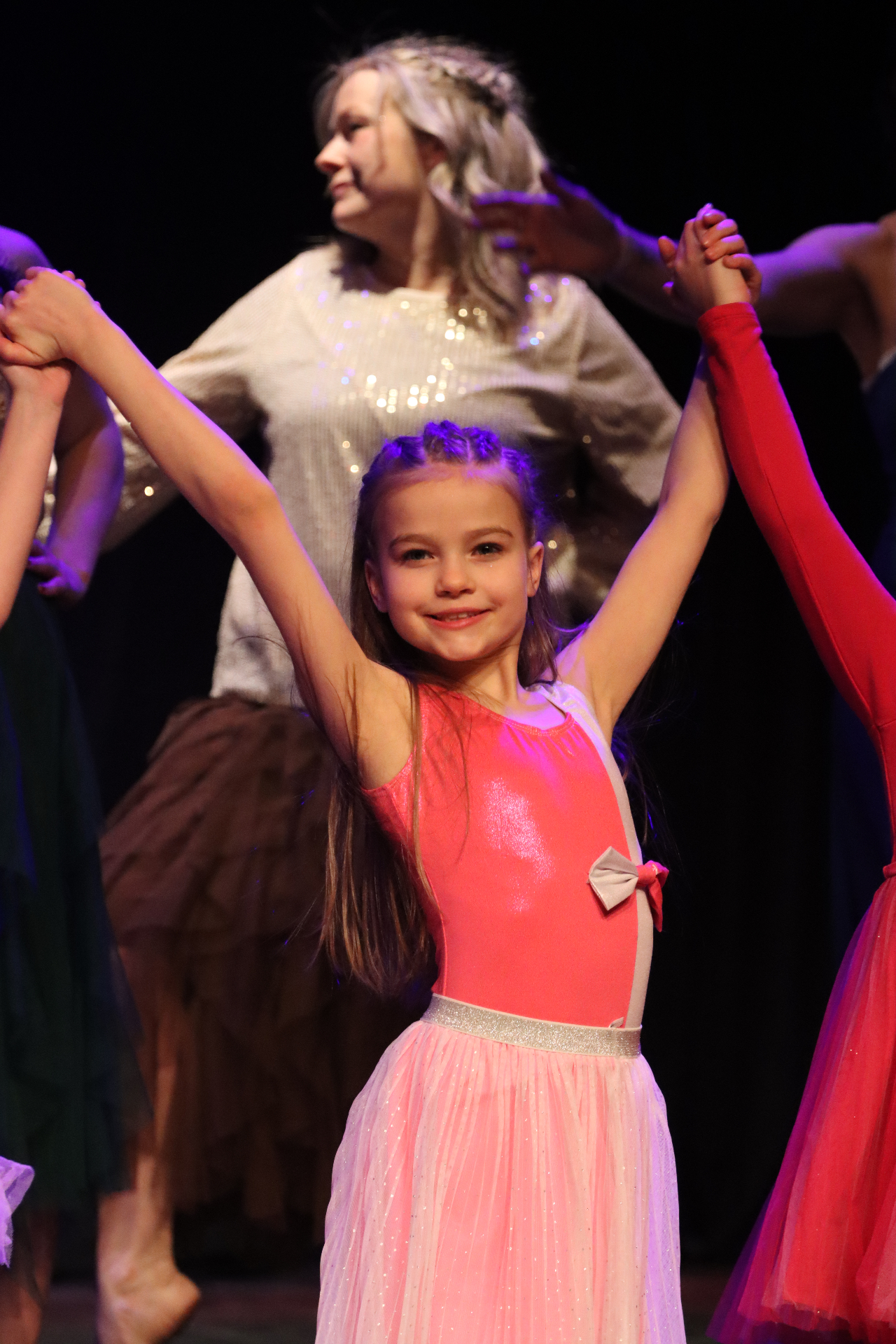 Petite danseuse en justaucorps rose, bras levés et sourire radieux