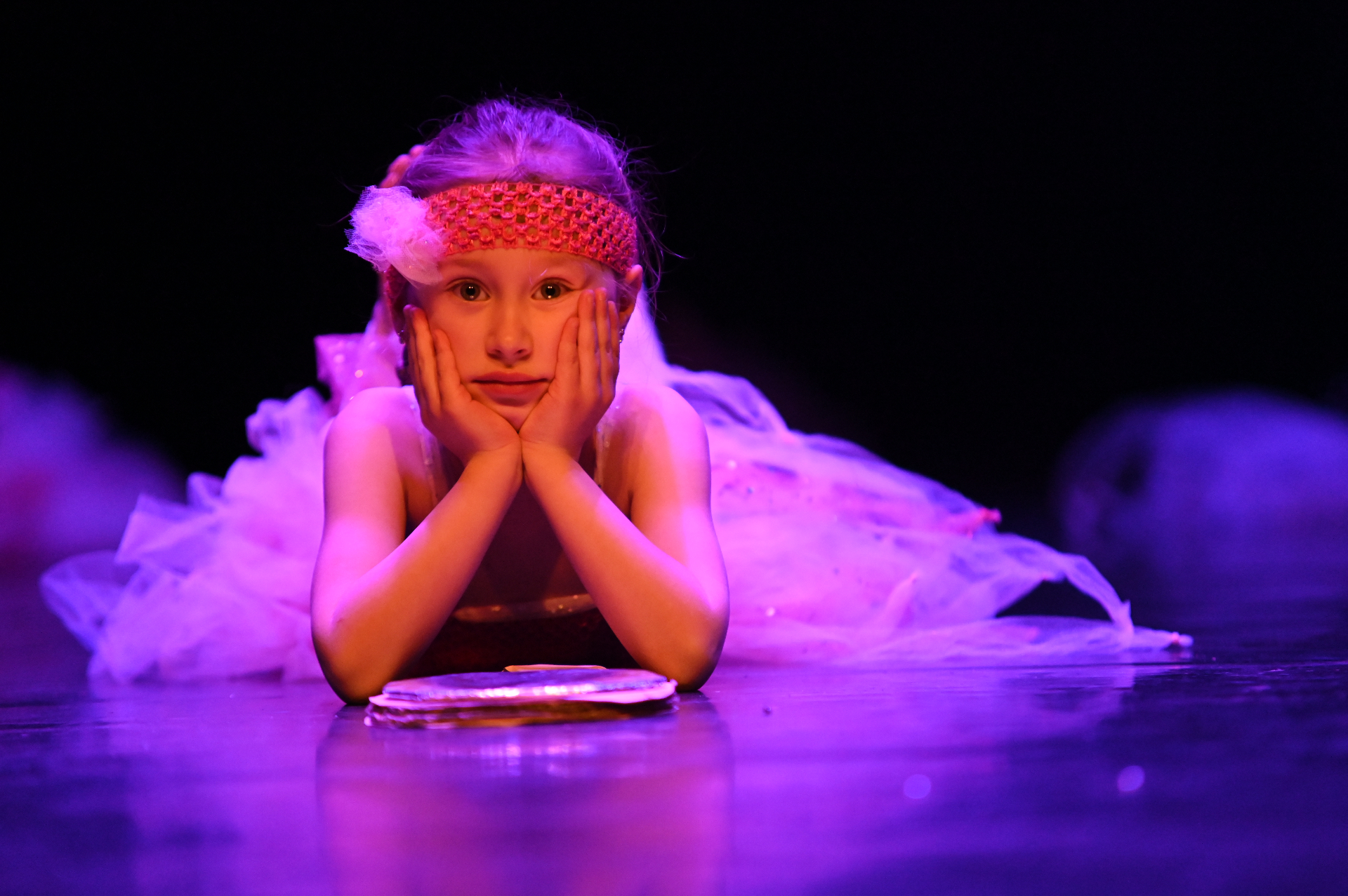 Petite fille en tutu rose allongée sur scène, lumière mauve
